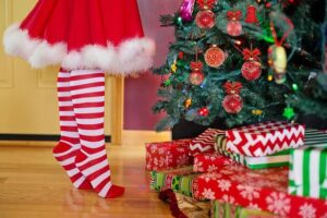 Une fillettes aux chaussettes rayée rouge-blanc, devant un sapin de noël avec des cadeaux aux pieds