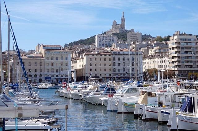 Photo du Vieux-Port de Marseille avec la basilique Notre-Dame de la Garde au loin sur un sommet
