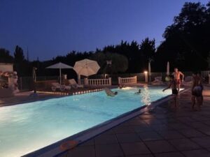 Des personnes sont au bord d'une piscine éclairée, à la tombée de la nuit