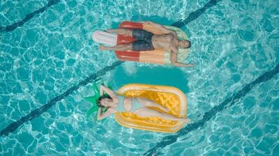 2 adultes sont allongés face au soleil sur des bouées, posées sur une piscine