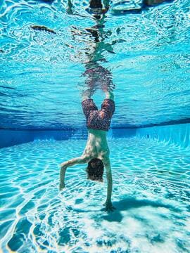 Un enfant de dos, plonge au fond d'une piscine et touche le fond avec sa main