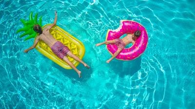 2 enfants sont allongés sur des bouées, posées sur une piscine